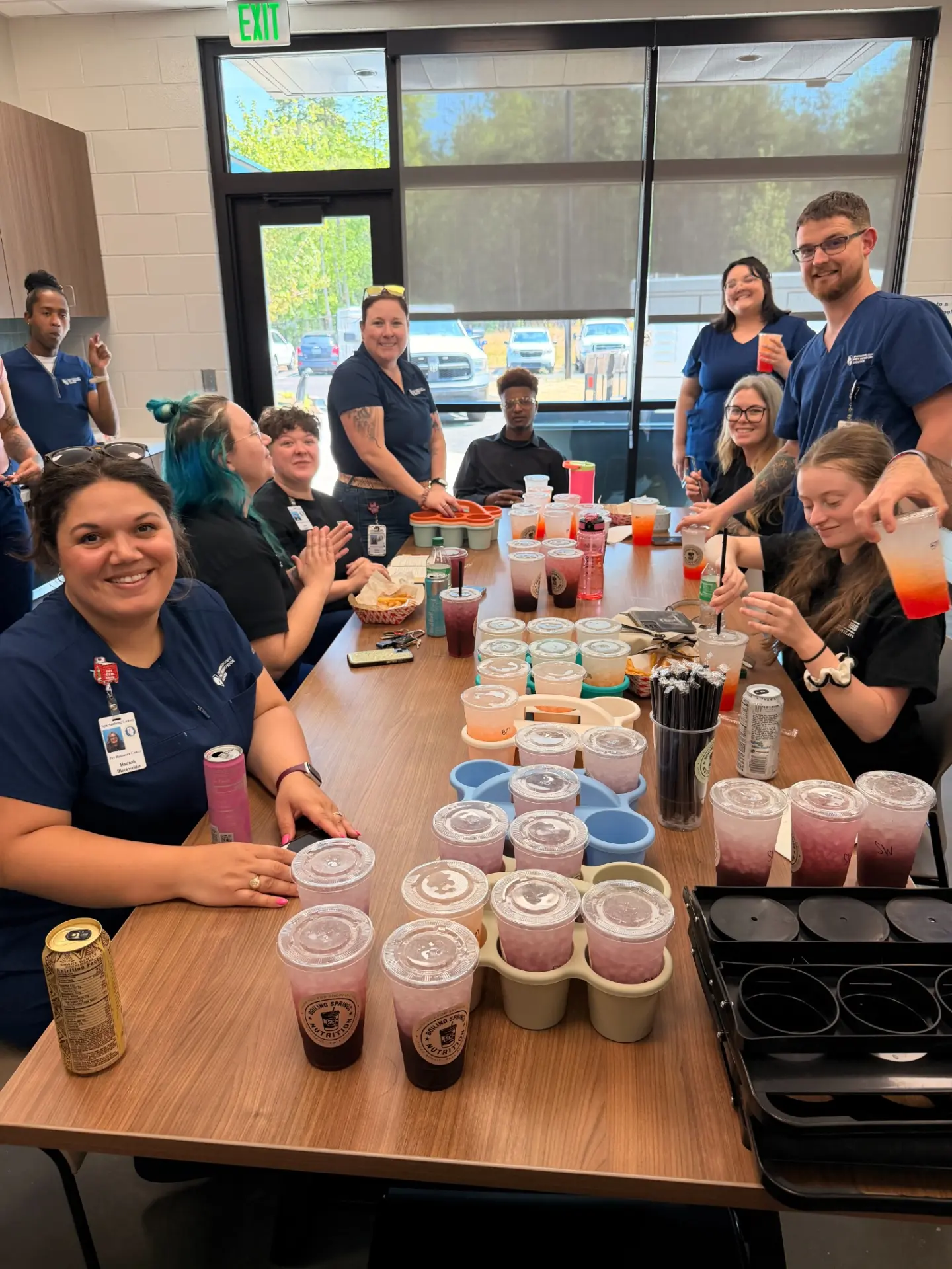 A group of local workers gathered around a table full of BSN drinks, celebrating together
