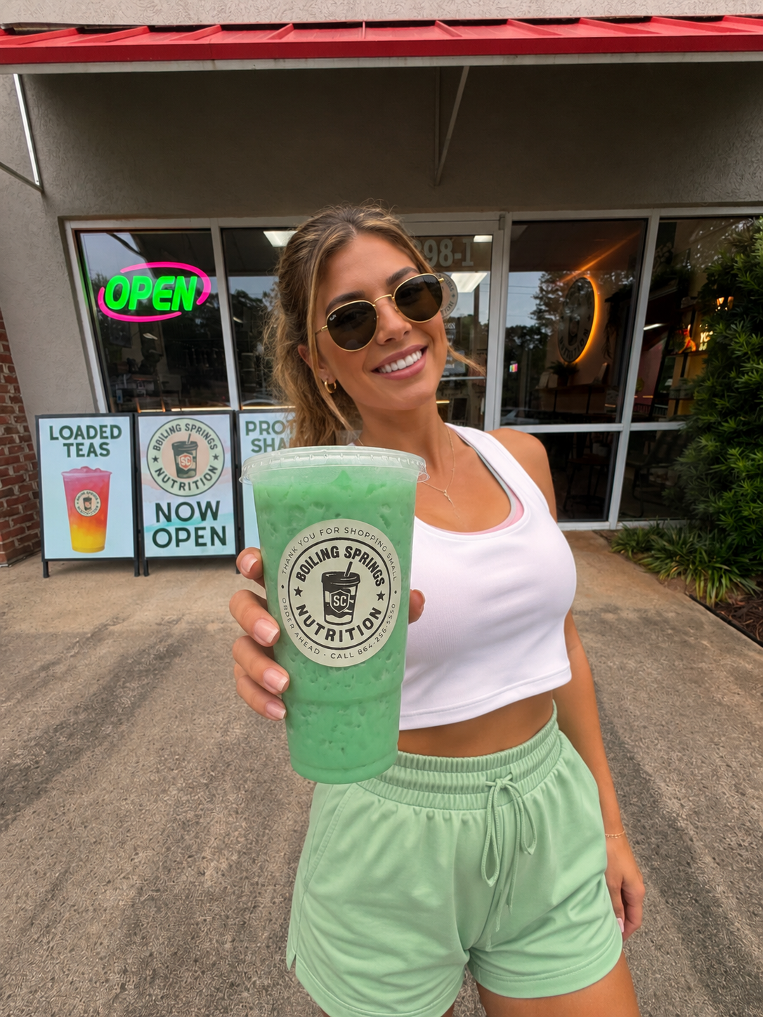 A woman outside Boiling Springs Nutrition holding a large green BSN drink